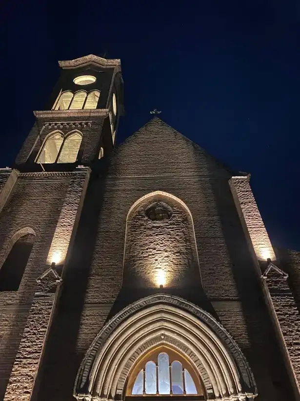 La fachada del templo iluminada de noche, con el rosetón encendido